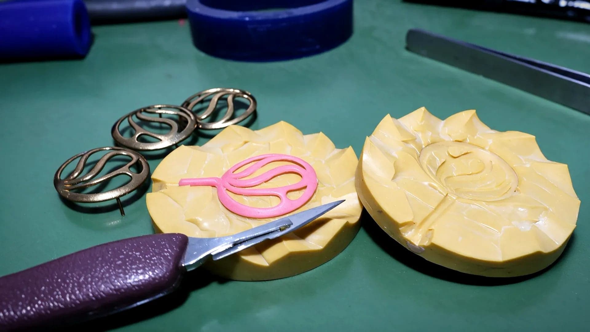 A rubber mold opened in two halves, with a fresh wax copy inside one and cast brass pieces beside it
